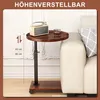 A small, round, wooden side table with a black metal frame and wheels is placed next to a cream-colored sofa. The table has a radio and a glass of drink on it. A graphic indicates the adjustable height of the table. Produktbild-Vorschau