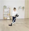 A young boy is playing with a toy vacuum cleaner in a room with shelves. Produktbild-Vorschau