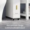 A close-up view of a slim white cabinet with a yellow handle, placed on a grey floor with wheels. The cabinet is next to a white shelf unit with folded towels. Náhľad obrázku produktu