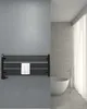 A black towel warmer mounted on a gray wall, with a white towel draped over it. A modern white bathtub and a chrome faucet are visible in the background. Produktbild-Vorschau