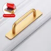 A gold-colored cabinet handle with a self-adhesive backing is shown on a white surface. Podgląd zdjęcia produktu