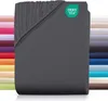 A folded dark gray fitted sheet is shown in the foreground, with a stack of sheets in various colors visible in the background. Produktbild-Vorschau
