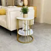 A round side table with two shelves is placed next to a sofa in a living room. Produktbild-Vorschau