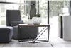 A modern living room setting with a chair, ottoman, coffee table with planters, and decorative cylindrical objects in the background. Náhled obrázku produktu