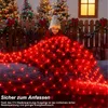 A child is playing with a net of red Christmas lights in a snowy outdoor setting with decorated Christmas trees. Produktbild-Vorschau