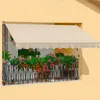 A balcony with a beige awning, decorated with colorful flowers in planters and a black metal railing. Produktbild-Vorschau