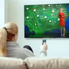 A woman is sitting on a couch holding a remote control and watching a weather forecast on a large TV screen. Voir les images du produit