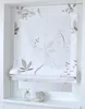 A white Roman blind with a subtle floral pattern is shown hanging in a window frame, with two small decorative items on the windowsill below. Produktbild-Vorschau