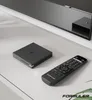 A black media streamer box and its remote control are placed on a white surface in front of a television. Anteprima dell’immagine prodotto