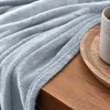 A close-up view of a light blue fluffy blanket draped over a wooden surface, with a portion of a wooden tray and a cup visible on the right. Produktbild-Vorschau