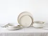 A set of ceramic plates and bowls with gold cutlery, arranged on a white tablecloth. Produktbild-Vorschau