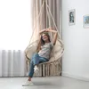 A woman is relaxing in a hanging chair in a room with curtains and framed pictures on the wall. Voir les images du produit