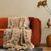 A plush beige blanket draped over an orange sofa, with decorative vases and dried flowers on a side table. Produktbild-Vorschau