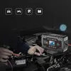 A person is working on a car engine, with a battery charger in the foreground. Náhled obrázku produktu