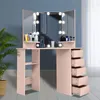 A pink vanity table with a tri-fold mirror and LED lights, set against a blue wall with a plant in a basket to the left. Voir les images du produit