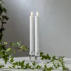 Two white LED taper candles in clear glass candle holders, surrounded by green ivy branches, on a white surface against a light gray background. Podgląd zdjęcia produktu