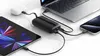 A black power bank is charging a laptop, a tablet, and a smartphone simultaneously, with a white charging case for earbuds connected to the power bank. Podgląd zdjęcia produktu