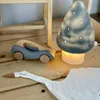 A wooden toy car and a mushroom-shaped lamp are placed on a wooden surface, with a white fabric resembling a swan's neck in the foreground. Produktbild-Vorschau