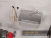 A utility sink with a faucet mounted on a tiled wall, with a towel hanging nearby and a lawnmower in the foreground. Produktbild-Vorschau