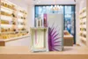 A perfume bottle and its box are displayed on a wooden surface in front of shelves stocked with perfume bottles. Produktbild-Vorschau