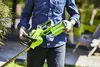 A person holding a green hedge trimmer in a garden setting. Podgląd zdjęcia produktu