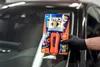 A hand wearing a black glove holds a product package in front of a car windshield. Produktbild-Vorschau