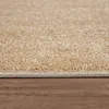 A close-up view of a beige carpet with a wooden floor. Produktbild-Vorschau
