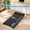 A compact treadmill placed on a wooden floor under a standing desk. Produktbild-Vorschau