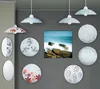 A collection of decorative ceiling lights and wall sconces arranged on a gray wall, with a framed seascape artwork in the center. Produktbild-Vorschau