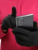 A person wearing black gloves and a pink jacket is holding a smartphone. Produktbild-Vorschau