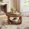 A round coffee table with a basket of books on its lower shelf, placed in a living room setting with a fireplace and curtains. Anteprima dell’immagine prodotto
