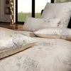 A close-up view of a bed with patterned bedding and pillows, with a window and a lamp in the background. Produktbild-Vorschau