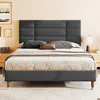 A bed with a dark gray upholstered headboard and frame, set in a bedroom against a pale orange wall. Náhled obrázku produktu