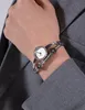 A close-up shot of a woman's wrist wearing a silver Guess watch with a white face and black accents. Produktbild-Vorschau