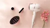 A white Philips hair dryer with rose gold accents is displayed on a light pink background, alongside three pink attachments. A small bouquet of pink flowers is also present. Náhled obrázku produktu