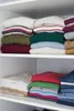 Neatly folded clothes are stacked on white shelves in a closet. Produktbild-Vorschau