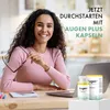 A woman is sitting at a desk with a laptop and a product box and bottle in front of her. Produktbild-Vorschau
