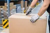 A person in a warehouse is using a utility knife to open a cardboard box. Anteprima dell’immagine prodotto