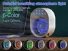 A small portable air cooler with various light color options displayed in circular previews at the bottom of the image. The main product is shown with a blue light effect, and a laptop and mouse are in the background. Produktbild-Vorschau