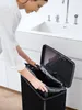 A woman is putting a black trash bag into a black trash can. Produktbild-Vorschau