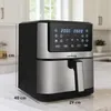 A black and silver air fryer is placed on a countertop in a kitchen setting. Voir les images du produit