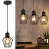 A trio of black industrial-style pendant lights hangs above a wooden dining table with decorative vases and plants. Produktbild-Vorschau