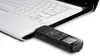 A black Sony digital voice recorder is plugged into the side of a white laptop. The recorder has a small screen and buttons. Náhľad obrázku produktu
