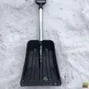 A black snow shovel with a silver handle is lying on a surface of snow. Náhled obrázku produktu