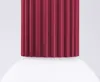 A close-up view of the top part of a burgundy-colored, fluted light fixture, resting on a white surface. Produktbild-Vorschau
