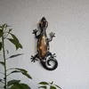 A decorative solar-powered gecko light is mounted on a textured wall, with a plant in the foreground. Produktbild-Vorschau