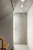 A modern interior hallway with concrete walls and ceiling, featuring recessed ceiling lights and a wooden handrail for stairs. Produktbild-Vorschau