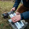 A person assembling a stainless steel grill outdoors on grass. Produktbild-Vorschau