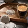A close-up shot of coffee pods and a glass of espresso on a wooden tray. Produktbild-Vorschau