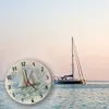 A clock with a painting of two sailboats on it is placed in the foreground, with a larger sailboat in the background on the water. Produktbild-Vorschau